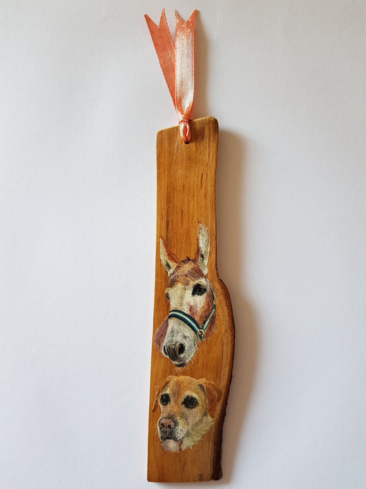 A wooden bookmark with a hand-painted portrait of a donkey and a dog. The bookmark is tied with a pink ribbon.