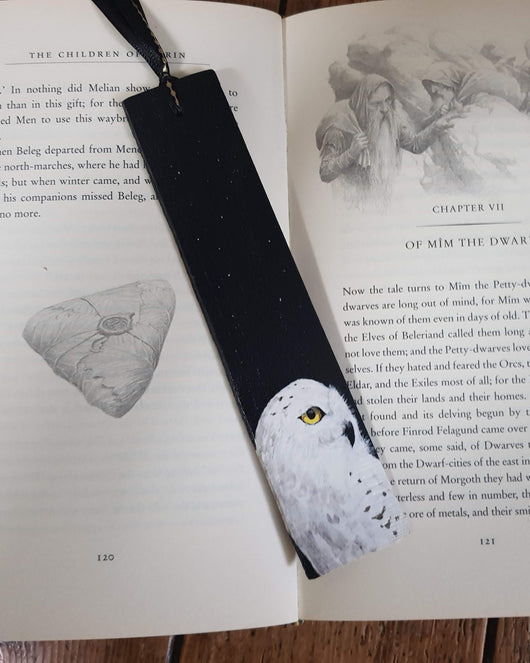 A black bookmark with a hand-painted snowy owl illustration placed in an open book. The book is open to Chapter VII of The Children of Húrin.