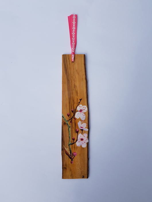 A wooden bookmark with a hand-painted illustration of a cherry blossom branch. The bookmark is tied with a pink ribbon.